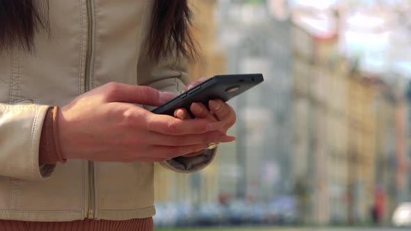 An Asian Woman Works on a Smartphone in a Street in an Urban Area - Closeup