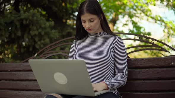 Young Woman Freelancer Working at Park Using Laptop Sitting on Bench