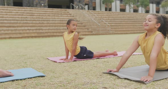 Video of focused diverse girls practicing yoga on mats in front of school