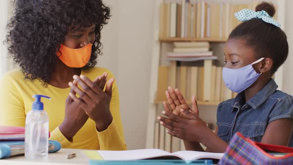 African american mother and daughter wearing face mask sanitizing their hands at home