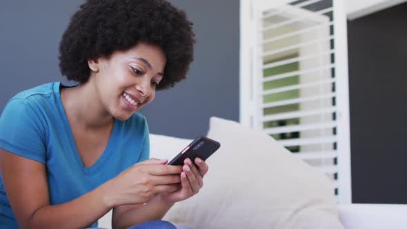 African american woman using smartphone while sitting on the couch at home