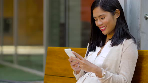 Asian Woman Using Smartphone Sitting on Bench