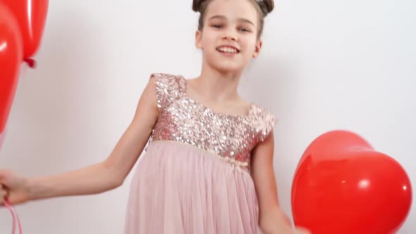 Teen Girl Dances Laughs with Red Balls of Hearts Near White Wall