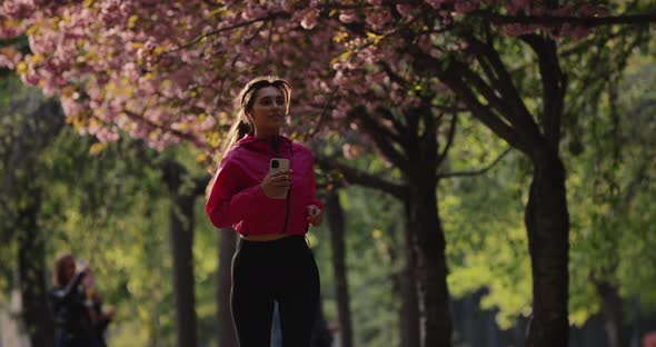 Pretty Sporty Woman Jogging in the Summer Park with Earbuds Listening to Music