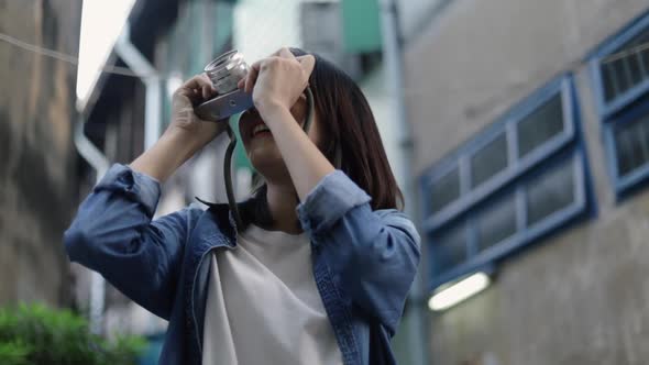 Asian woman traveler using a film camera taking a photo at a small street in Bangkok Thailand.