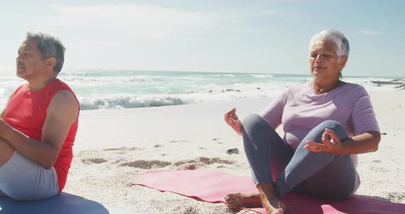 Relaxed hispanic senior couple practicing yoga on mats on beach