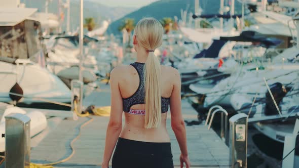 Back View of Slim Woman in Gym Outfit Walking in Yacht Port