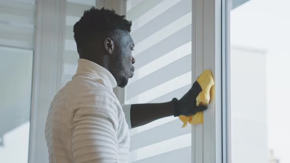 African Black Man Sanitizing Apartment. Spraying and Wiping the Window Frames