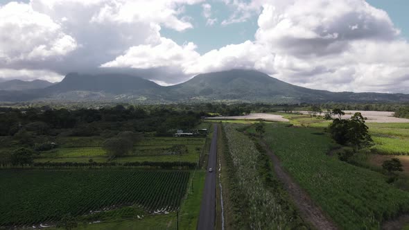 Aerial tracking shot in 4k following a car driving along straight country road with giant Arenal vol