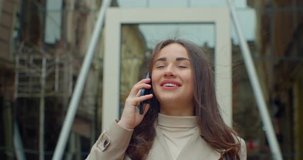 Happy Young Woman Talking on the Cell Phone While Walking Near Big Modern Office Building. Close Up.