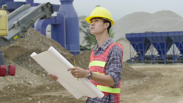 Architect Standing In Construction Site Looking At Blueprint