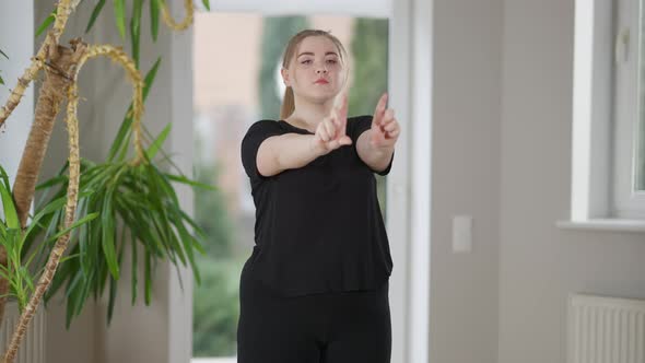 Portrait of Concentrated Confident Young Plussize Woman Warming Up Wrists Exercising Indoors