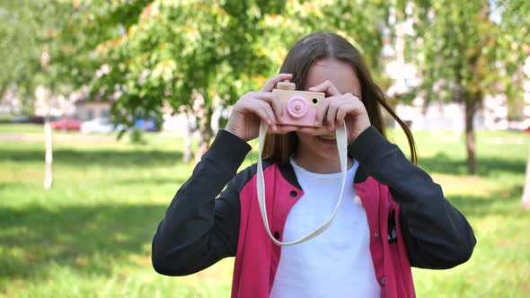 Girl 11 Years Old Takes Pictures with a Toy Wooden Pink Camera.