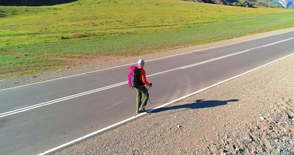 Flight Over Hitchhiker Tourist Walking on Asphalt Road. Huge Rural Valley at Summer Day. Backpack