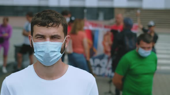 Portrait of rally activist in coronavirus mask among protesting crowd in city.