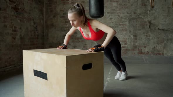 Athlete Young Woman Does Pushups on a Wooden Box in the Gym