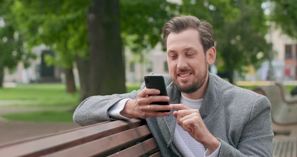 Young Man with Mustaches and a Beard is Sitting on a Bench Leaning with His Elbow on It in the