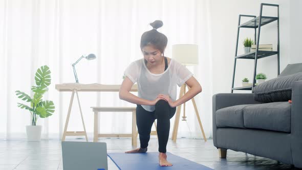Young lady exercises doing working out and using laptop to watching yoga video tutorial at home.