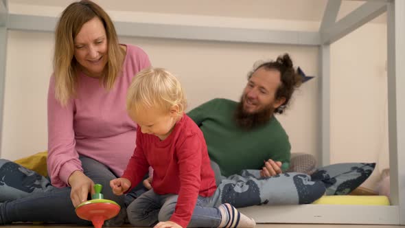 Father and mother showing spinning toy to Infant son at children room. alt