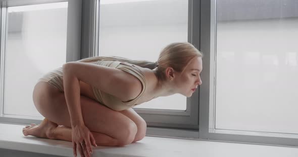 Attractive Young Blonde Woman Makes Acrobatic Gymnastic Tricks in Slow Motion on the Windowsill of