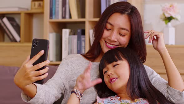 Asian mom and her kid are calling on smartphone. Both happy using cellphone for video call smiling m