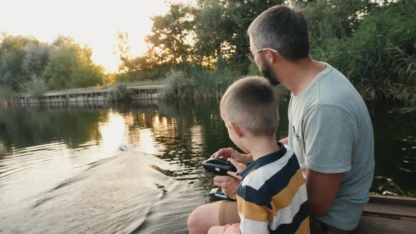 Father and Little Son Play with RC Toy Speedboat on the Lake