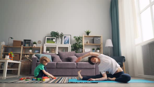 Loving Mom Practising Yoga Watching Her Son Playing with Bricks and Talking