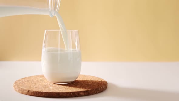 Pouring milk in glass from a bottle on a light neutral background with space for text