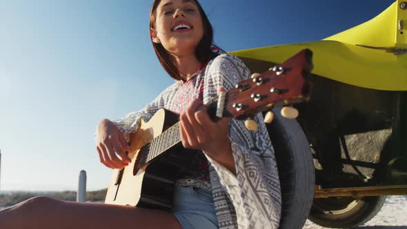 Happy caucasian woman sitting in beach buggy by the sea playing guitar