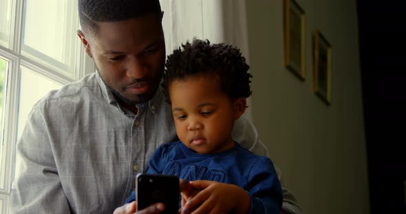 Front view of black father and son using smartphone in a comfortable home 4k