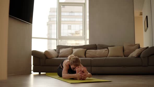 Slim Blonde Woman Sits on Mat Does Exercises and Stretches By Leaning Torso Forward at Morning in
