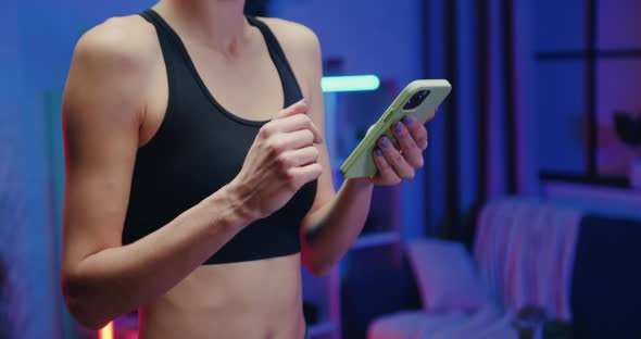 Woman in Black Top Stepping on Treadmill and Uses Her Mobile During Evening Home Workout