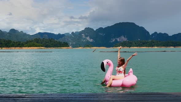 Woman Fun Dancing Raised Hands Up on Pink Inflatable Flamingo at Blue Lake