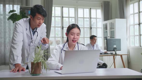 Two Asian Professional Physicians Talking, Consulting And Working On Laptop Computer