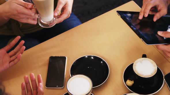 Friends using mobile phone and digital tablet while having cup of coffee