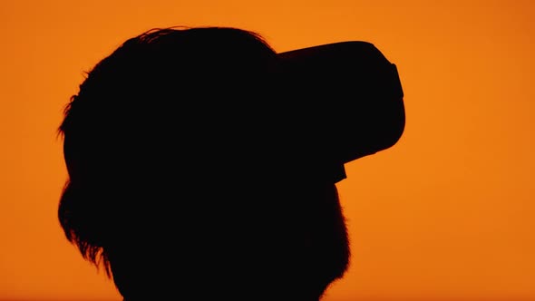 Close-up of a silhouette of a man's head wearing VR glasses against a color-changing background