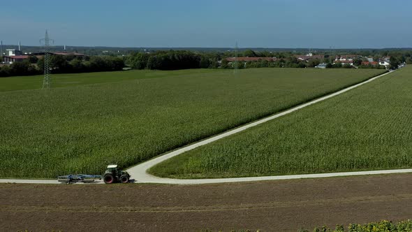 Aerial view at a tractor driving on a country road next to a growinggreen field with a village in th