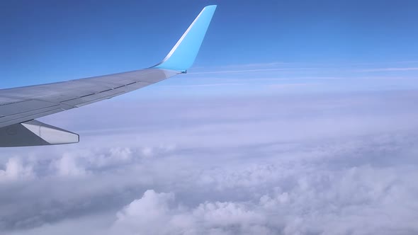 View of the Wing of a Flying Plane High in the Sky Through the Clouds in Sunny Weather