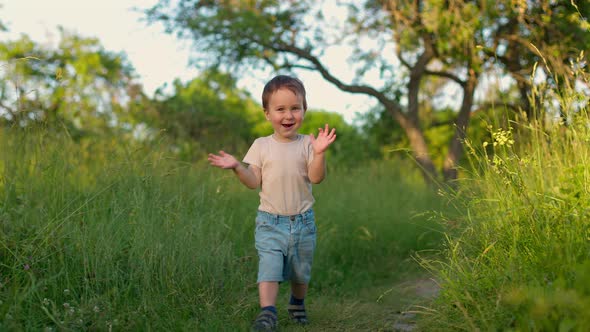 Cheerful Cute Baby Boy Runs Forward in a Green Garden