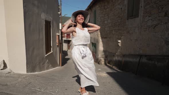 Wide Shot of Excited Woman in White Dress Spinning on Sunny Street in Ancient Town on Cyprus Smiling