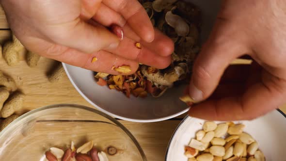 Close-up of men's hands peeling peanuts over bowls. Top view. Peeling an earthy peanut at home