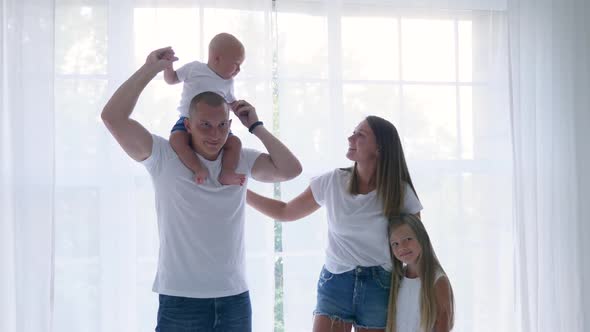 Family of Four Stands in a White Room Against