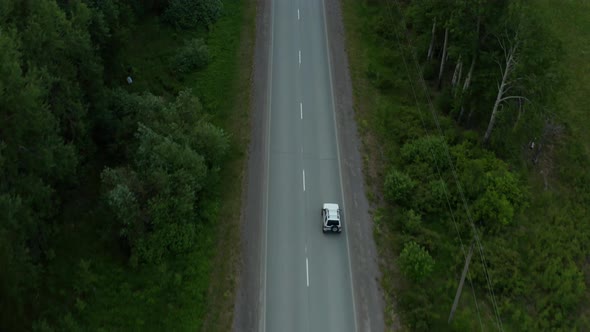 Aerial View of a Car Driving Along the Road Among Fields of Green Grass