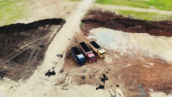 Aerial View of Large Trucks with Fresh Asphalt in Trailers for Road Construction at the Test Site