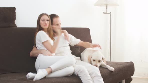 Lovely Caucasian Couple Sit on Sofa Wit Their Pet, White Dog