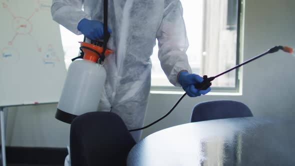 Mid section of health worker wearing protective clothes cleaning the office using disinfectant spray