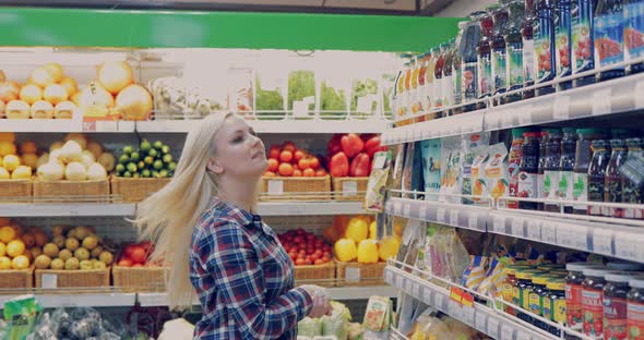 Attractive Woman is Walking Near the Supermarket Shelf and Selects the Products