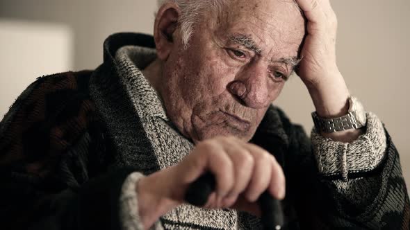 Thoughtful Pensioner Takes His Head with Hand and Keeps Other Hand on His Stick