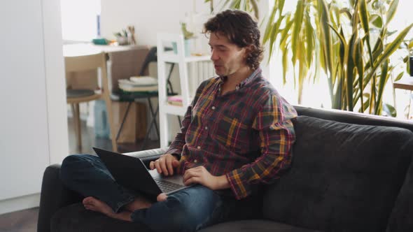 Happy adult man in a plaid shirt working on laptop and talking