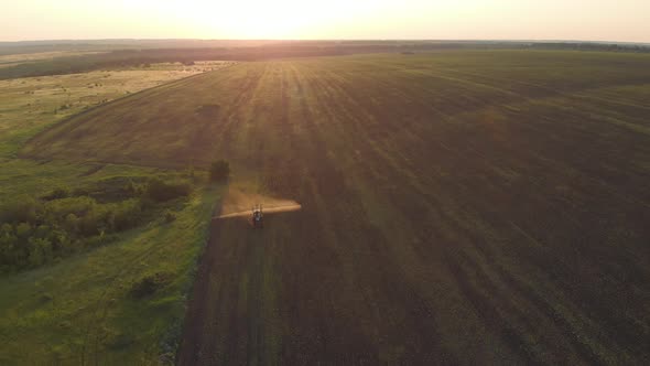 Aerial View of Farming Tractor Spraying on Field with Sprayer, Herbicides and Pesticides at Sunset